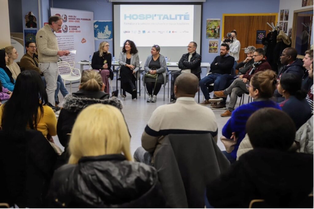 Photo de la visite de Madame la ministre Christie Morreale en janvier 2023. Les partenaires et stagiaires sont en cercle dans une salle du Monde des Possibles tandis que Didier Van der Meeren prend la parole.